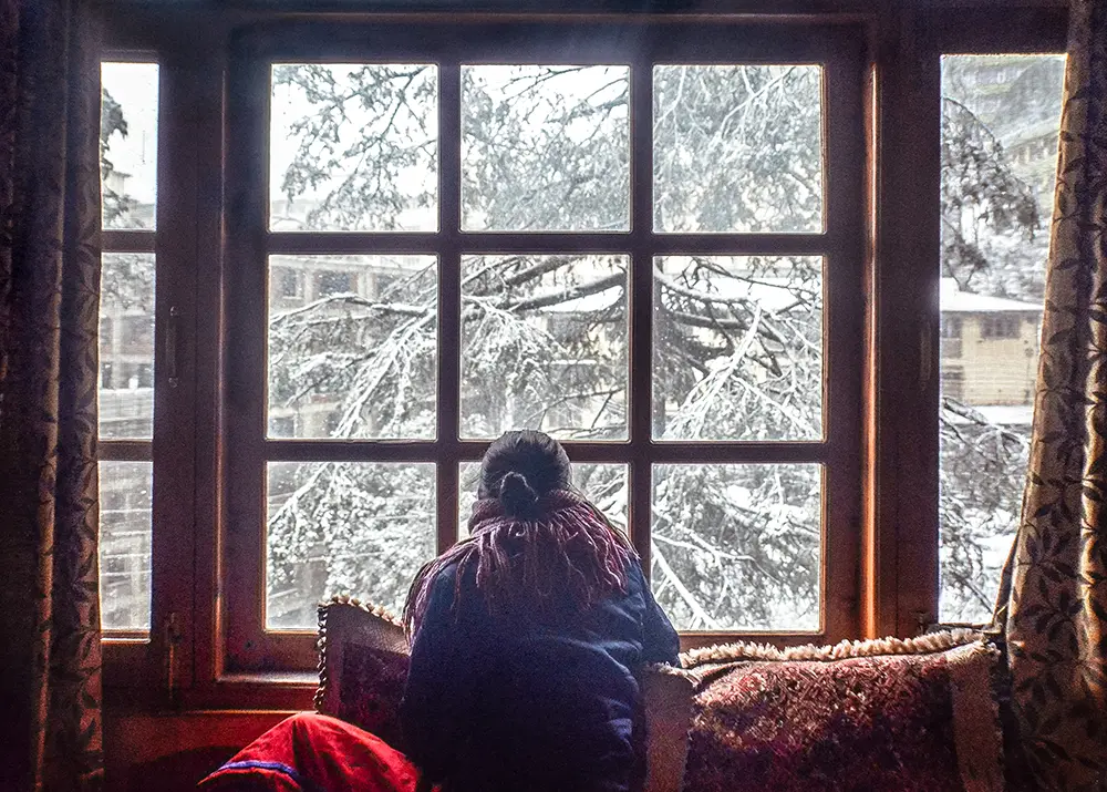 happy-guest-looking-at-snow-outside-window-at-kalawati-homes-shimla